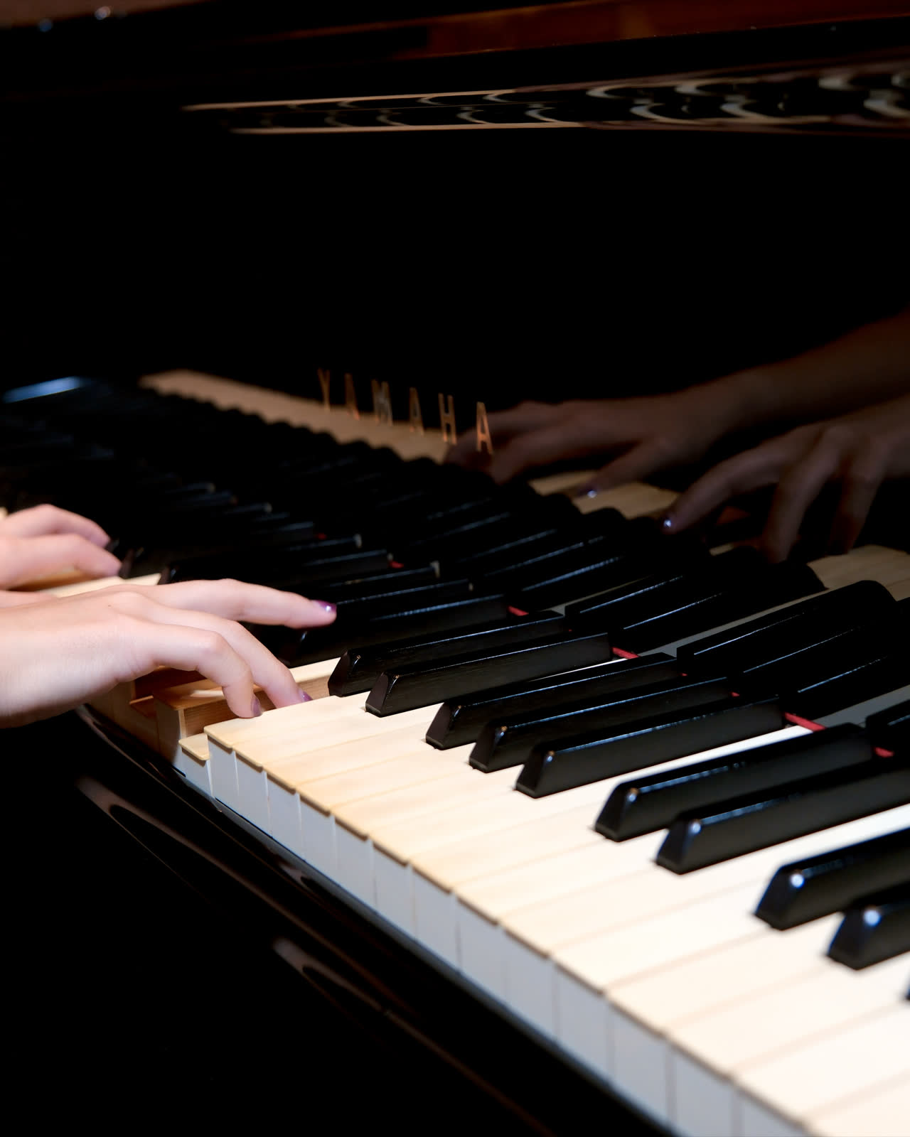 Two hands on the keys of the studio’s Yamaha upright, lit close against the dark case.