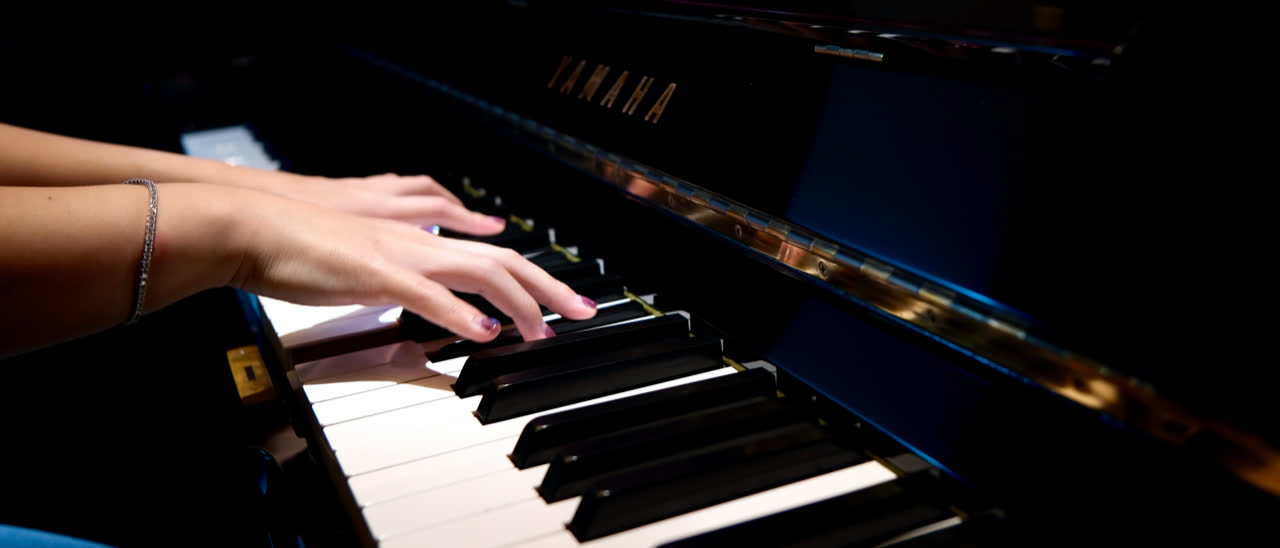 A hand on the keys of the Yamaha upright, lit close and low against the dark case.