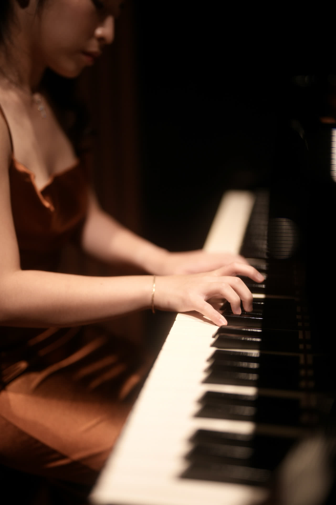 Sally Yapto's hands on the keys, lit from above in a darkened hall.