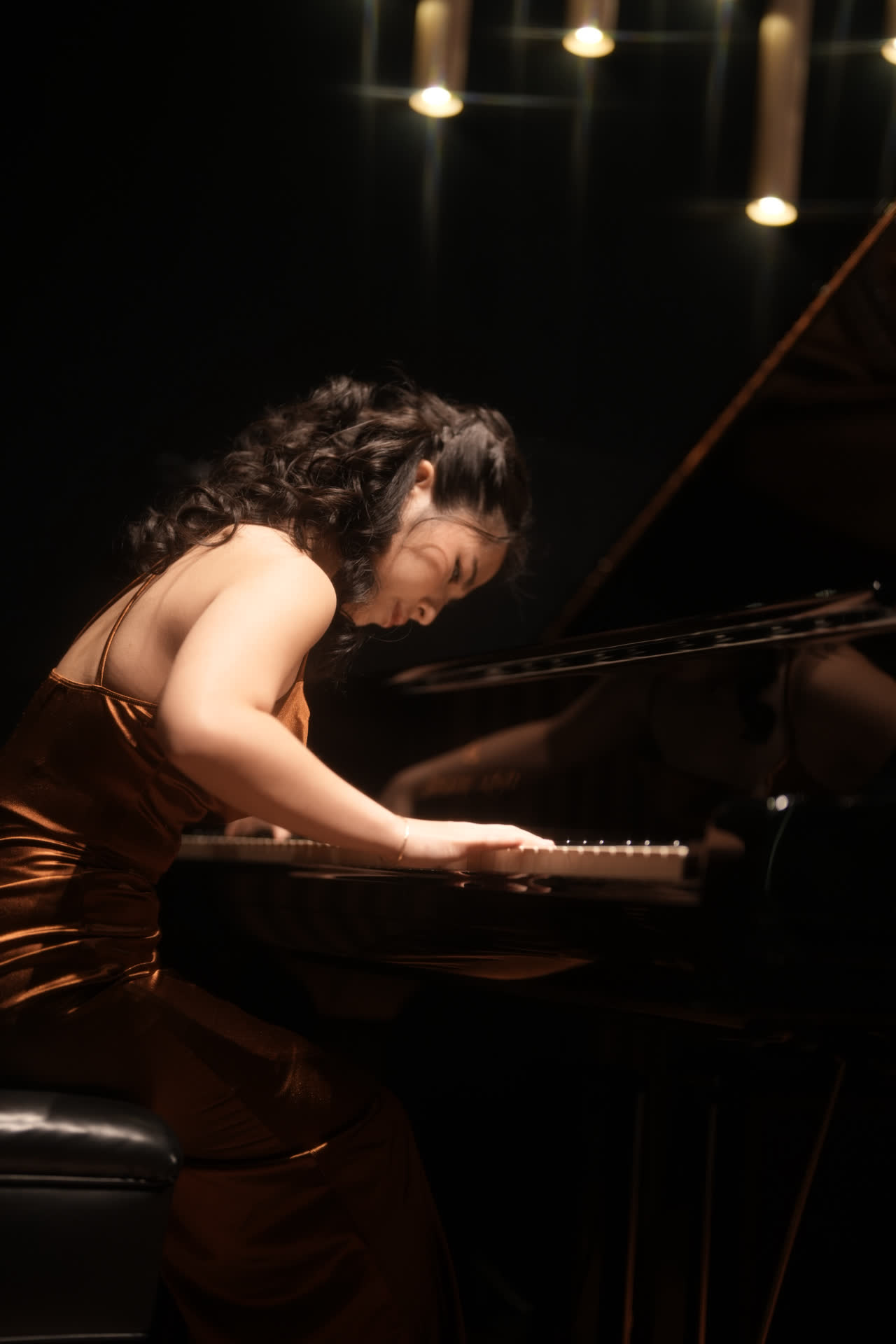 Sally Yapto performing, leaning into the keys under stage lights in a bronze gown.