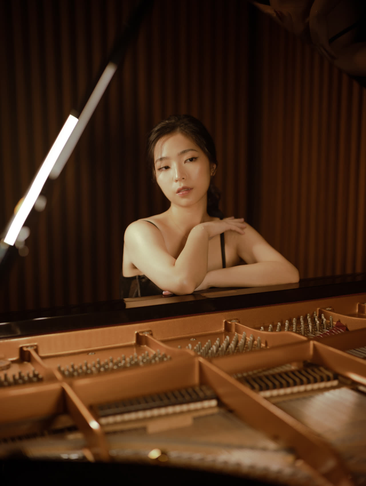 Sally Yapto resting her arms on the rim of the open grand piano, looking into the camera.