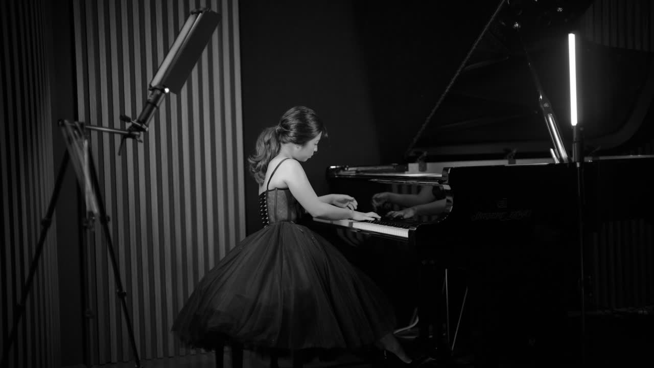 Sally Yapto at the grand piano in the studio, in a full black gown, photographed in black and white.