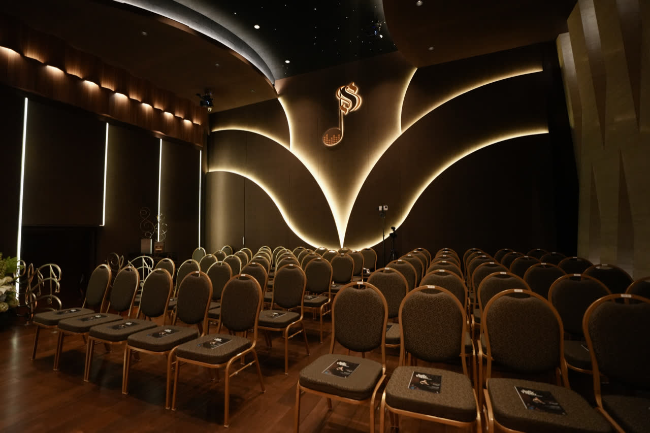 The hall's seating from the side, facing the backlit Symphony quaver on the wall, a microphone stand and a fixed camera in place.