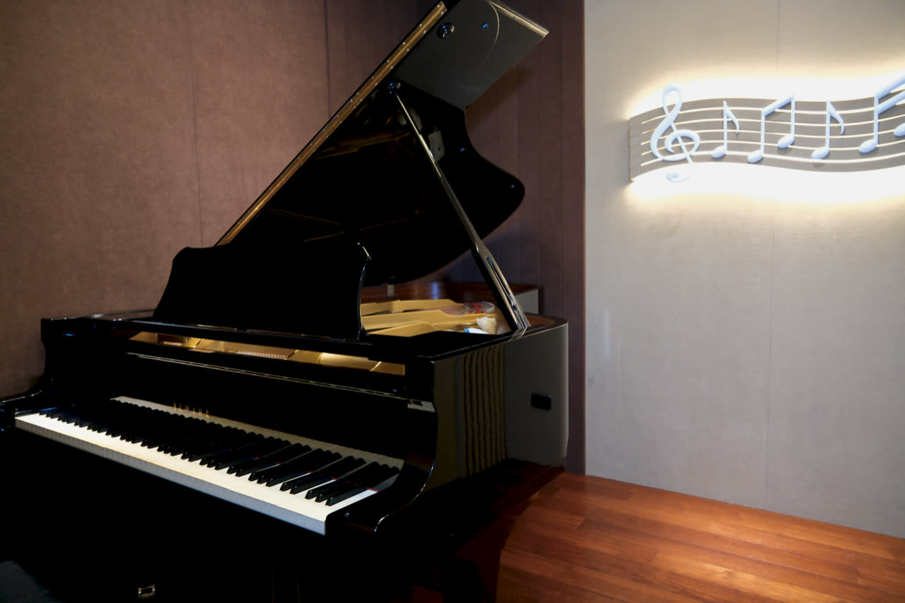 The Yamaha grand in the teaching room, lid open, beside a wall relief of a musical staff.