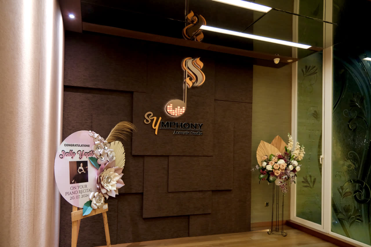 The studio entrance: the illuminated Symphony Acoustic Studio mark on a panelled wall beside glass doors.