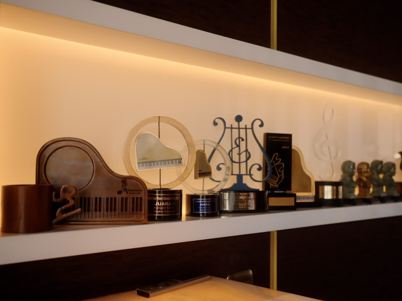 A lit shelf in the lounge holding piano-competition trophies and small musical figures.